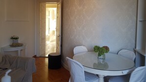 A dining area with a round table, white chairs, and a vase with flowers. There is a small side table with a decorative item and a vase. A door leads to another room. - Apartment Vesna (Lovran)