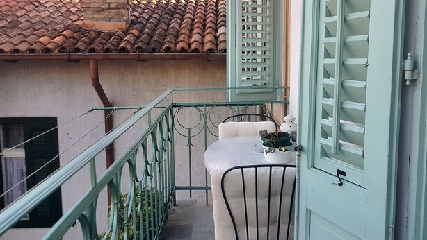 A balcony with a table and chairs, a potted plant, and a window with shutters. - Apartment Vesna (Lovran)