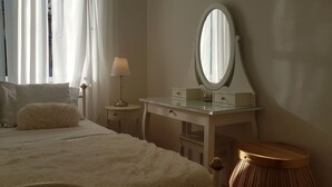A bedroom with a bed, a bedside table with a lamp, a dresser with a mirror, and a round wooden stool. - Apartment Vesna (Lovran)