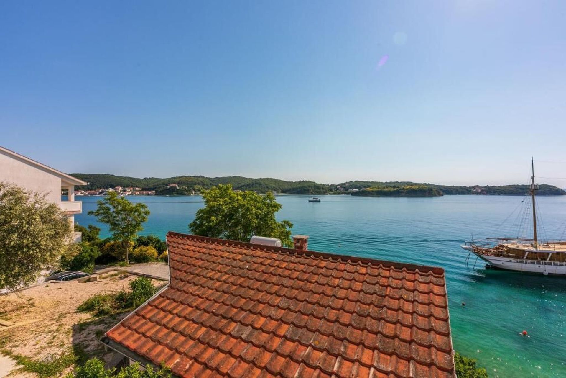 A coastal view with a tiled roof, a boat docked near the shore, and a clear blue sky.