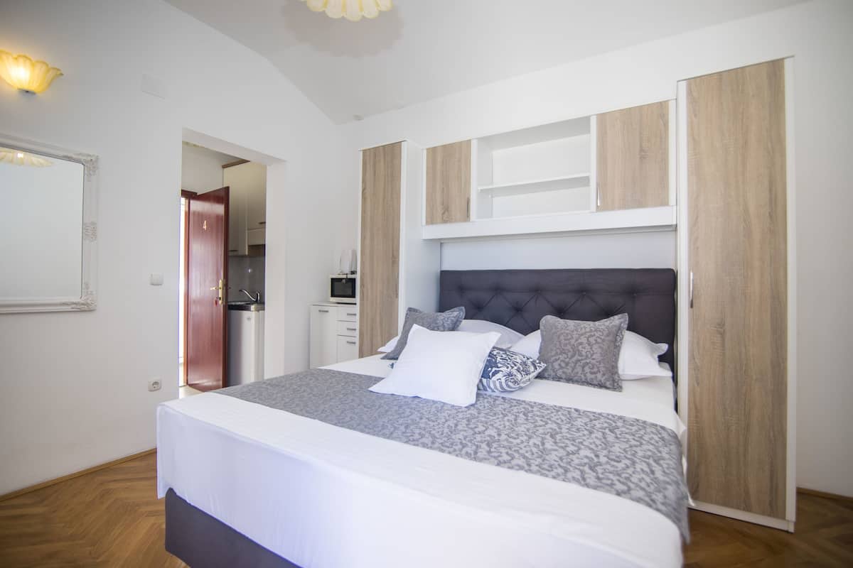 A modern bedroom with a large bed, built-in wooden cabinets, and a small kitchenette in the background.