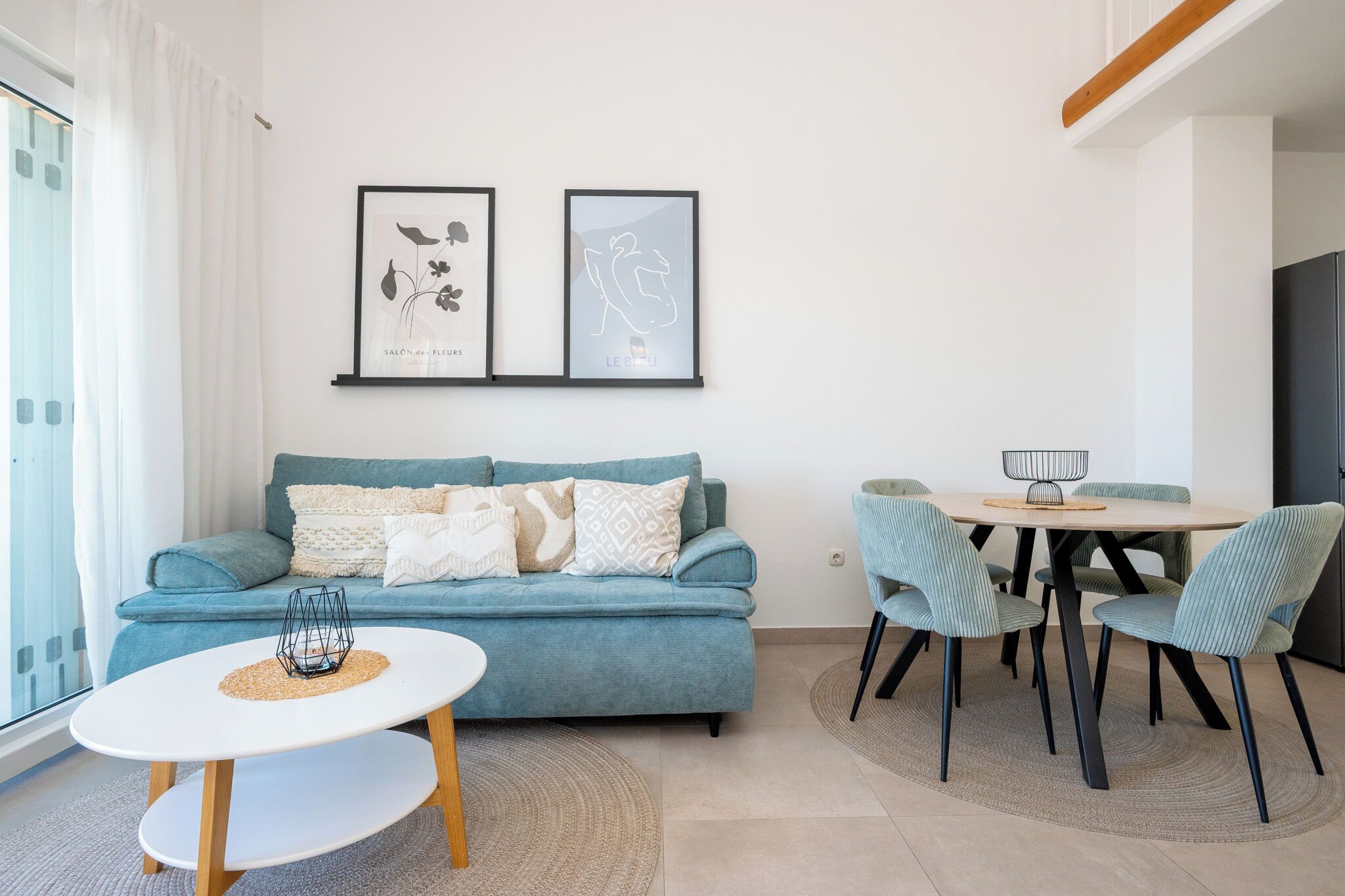 A modern living room with a blue sofa, a round white coffee table, and a dining area with a wooden table and striped chairs.