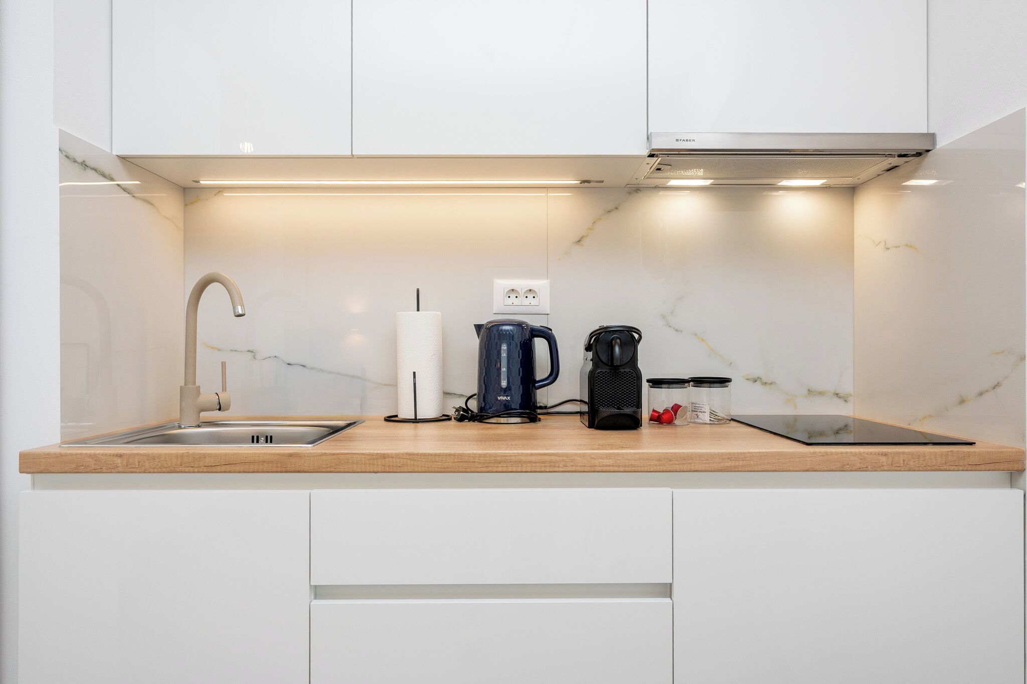 A modern kitchen with a built-in stove, a sink, and a countertop with a kettle, a coffee maker, and jars.
