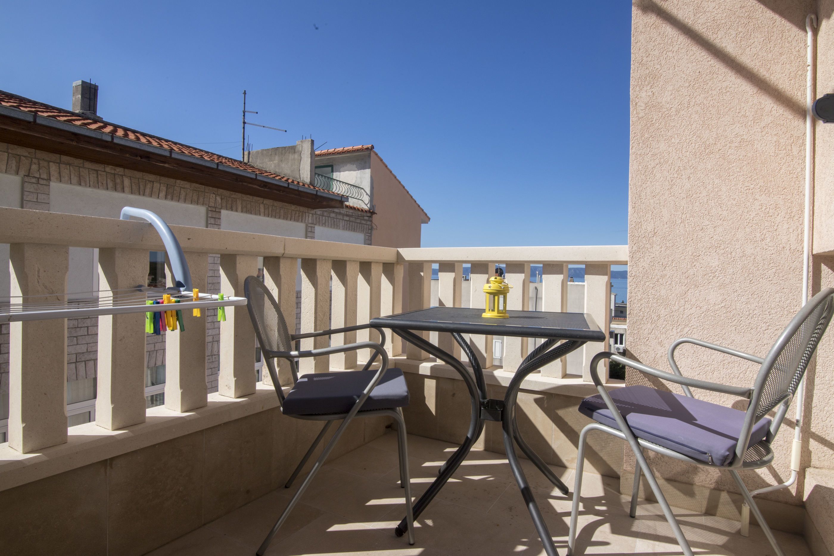 A balcony with a table and chairs, a yellow lantern, and a view of neighboring buildings.