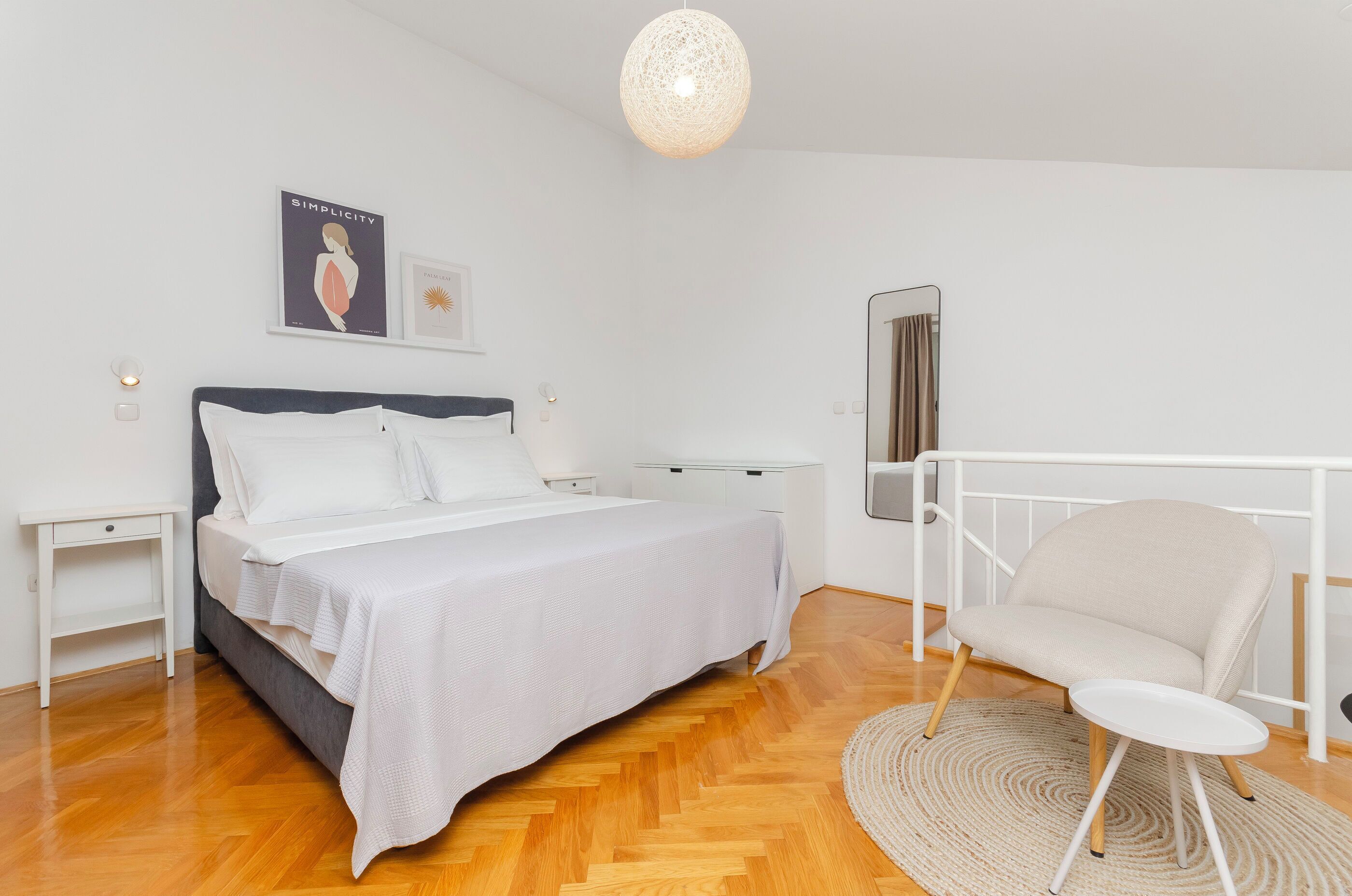 A bedroom with a bed, bedside tables, a chair, a hanging light fixture, and artwork on the wall.