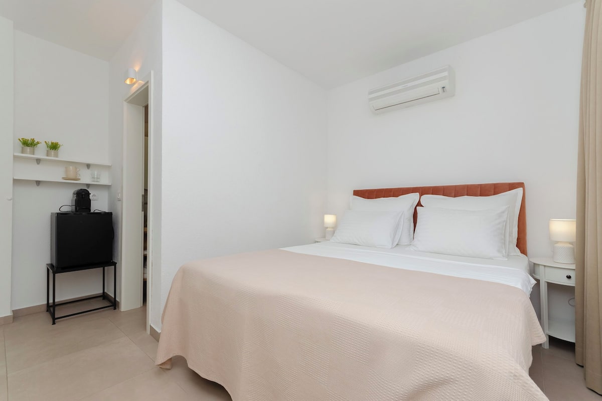 A neatly arranged hotel room with a bed, bedside tables, a TV on a stand, and a shelf with decorative items.