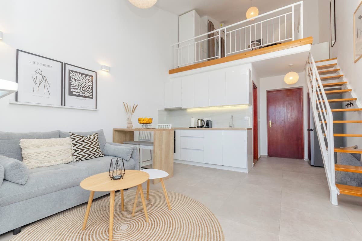 A modern apartment with a living area, kitchenette, and a staircase.
