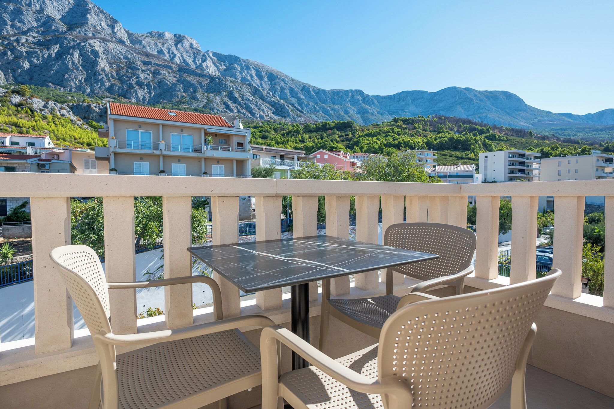 Un balcon avec une table et des chaises, donnant sur un paysage montagneux avec des bâtiments en arrière-plan.