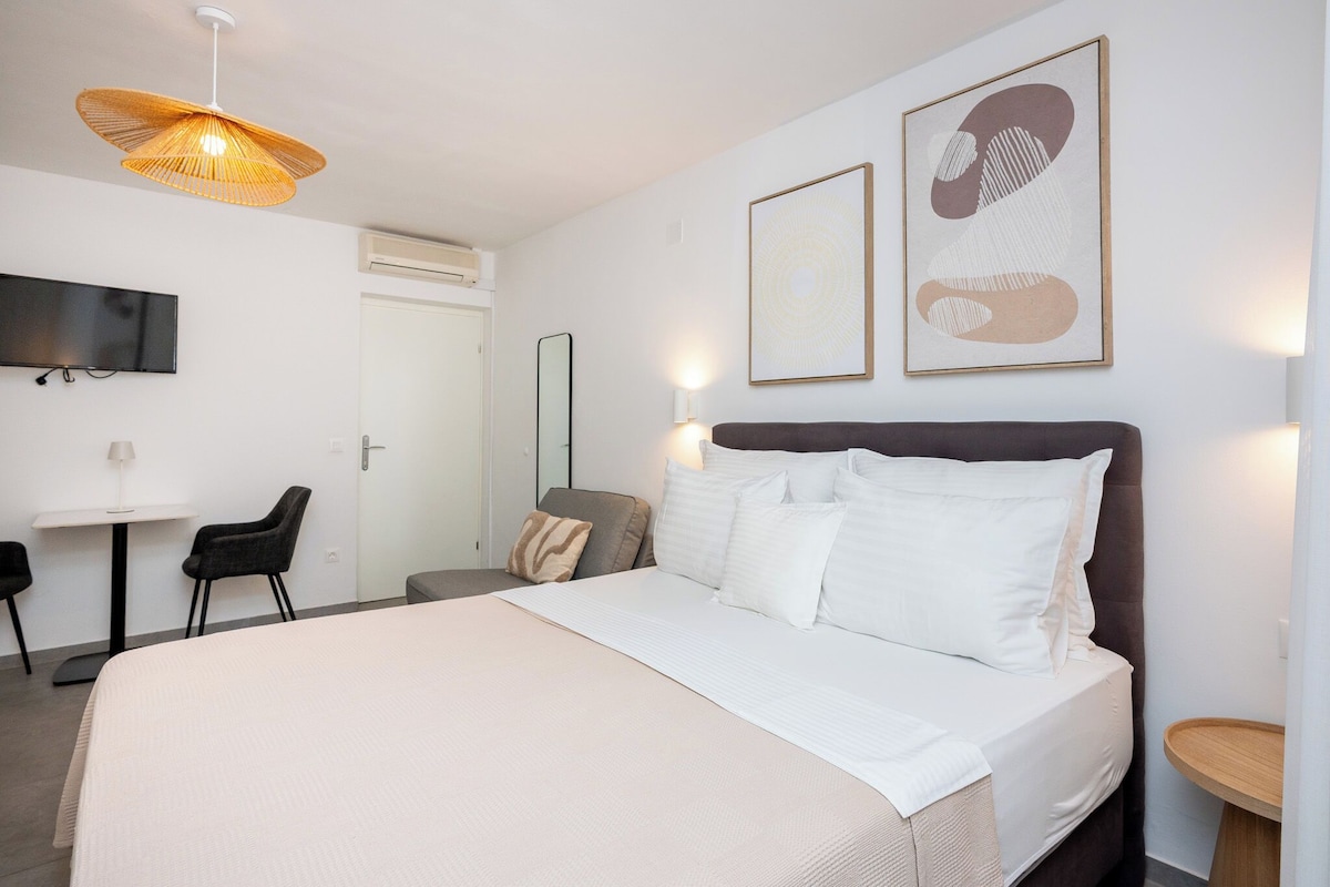 A hotel room with a bed, a desk, a chair, a TV, and artwork on the wall.