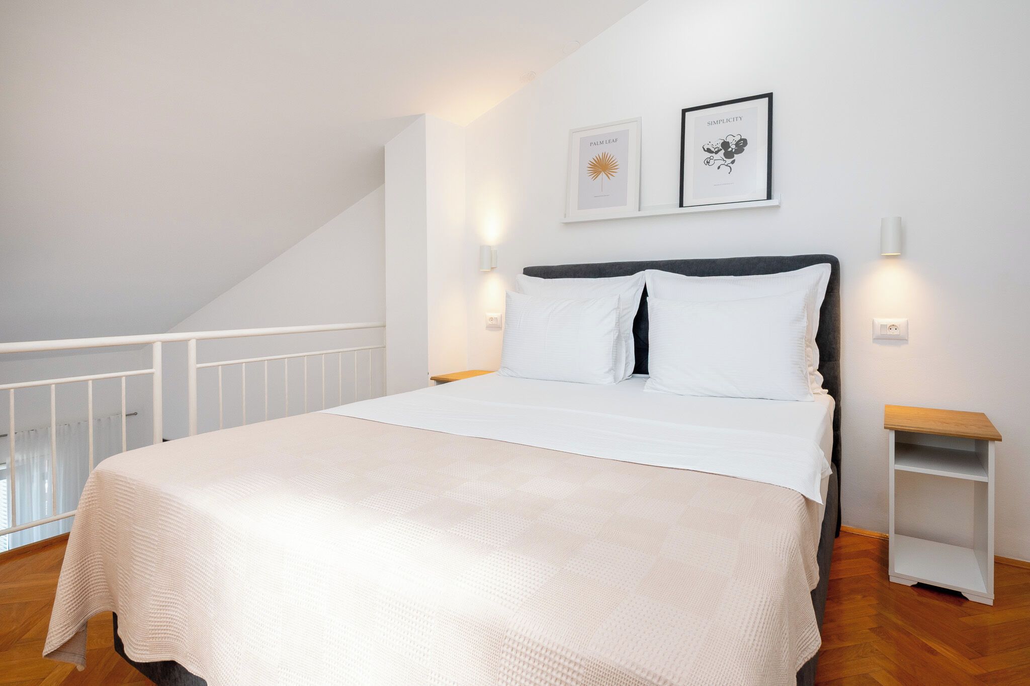 A bedroom with a bed, a nightstand, a wall-mounted light, and a framed picture.