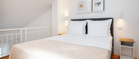 A bedroom with a bed, a nightstand, a wall-mounted light, and a framed picture.