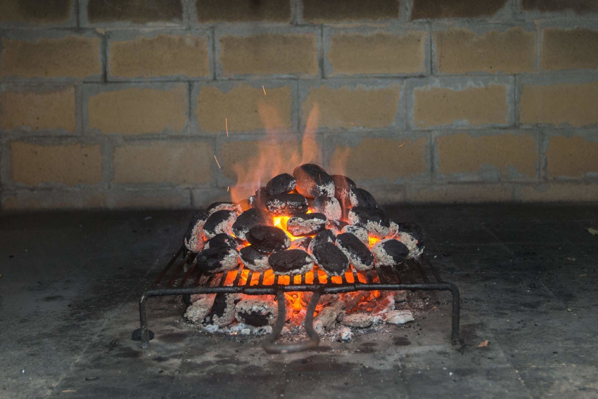 A charcoal grill with burning coals and visible flames, set against a brick wall background.