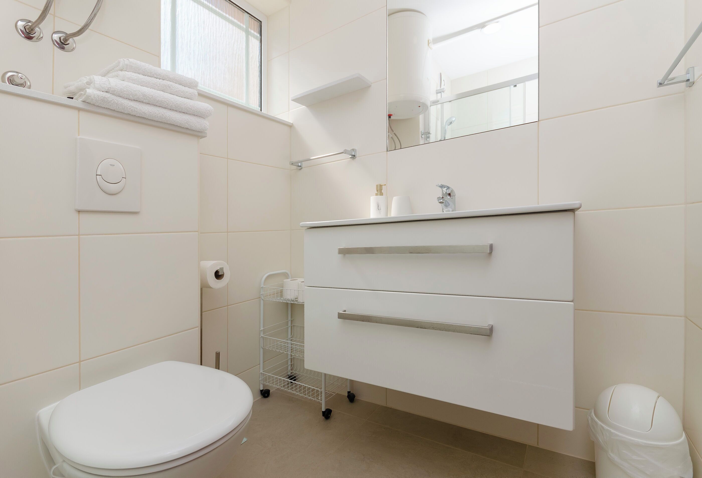 A modern bathroom with a toilet, a white sink with a mirror, and a towel rack.