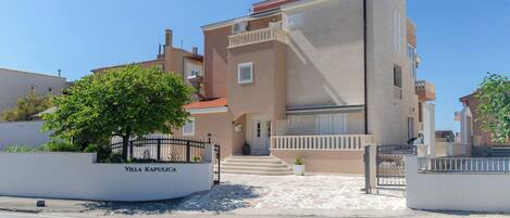 A modern villa with a beige facade, a red roof, and a gated entrance.