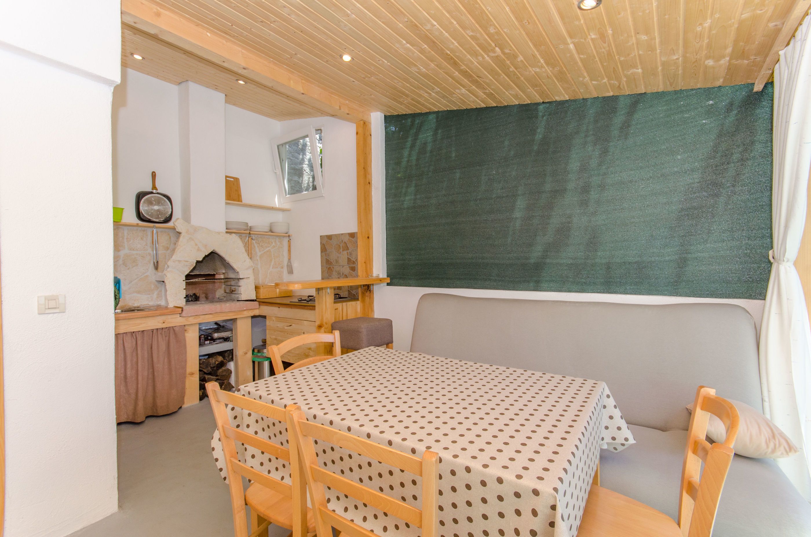 A cozy room with a wooden ceiling, a stone fireplace, a dining table with chairs, and a green curtain.