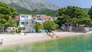 A coastal hotel with multiple buildings, a sandy beach, and clear turquoise water. - House Beach House Toma (Zivogosce)