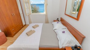 A bedroom with a wooden wardrobe, a bed with white linens, a window with a view of the sea, and a mirror on the wall. - House Beach House Toma (Zivogosce)