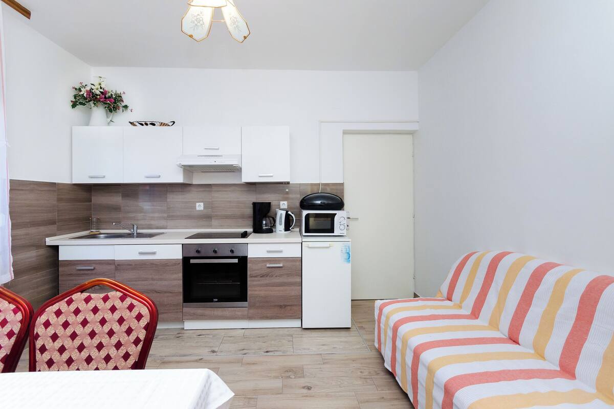 A compact living space with a kitchenette, a dining area with a table and chairs, and a striped sofa.