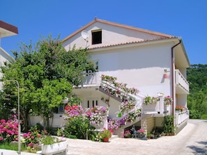 A two-story building with a balcony, surrounded by potted plants and flowers.
