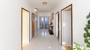 A hallway with white walls, a tiled floor, and doors leading to rooms. There is a ceiling light fixture and a plant on the right side. - Apartments Rezika (Palit)