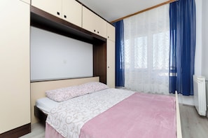 A bedroom with a bed, built-in wardrobe, and a window with curtains.