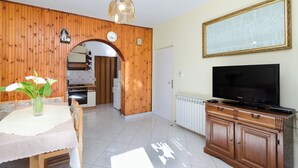 A kitchen with wooden walls, a dining table with a vase of flowers, a TV on a wooden cabinet, and a clock on the wall. - Apartments Rezika (Palit)