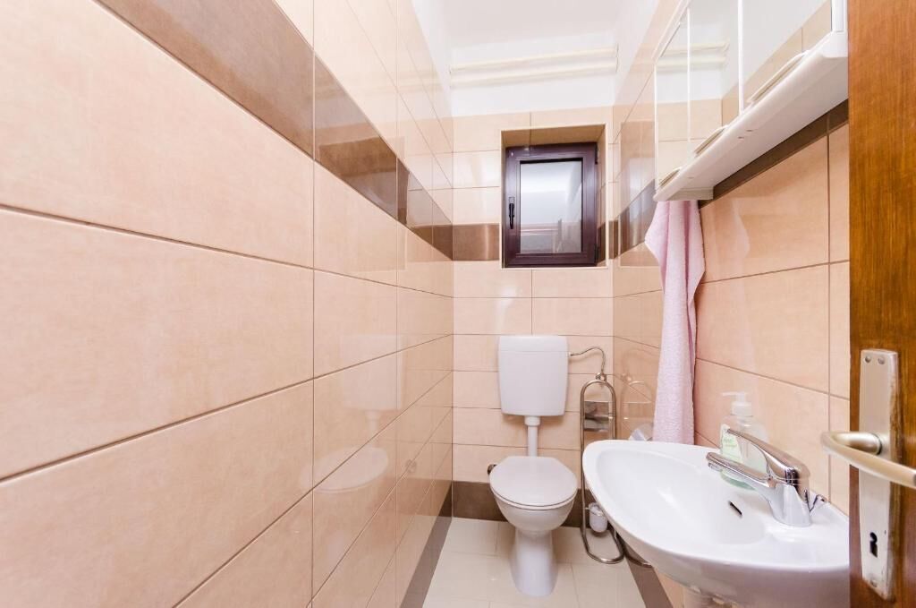 A small bathroom with a toilet, sink, and a window above the toilet.