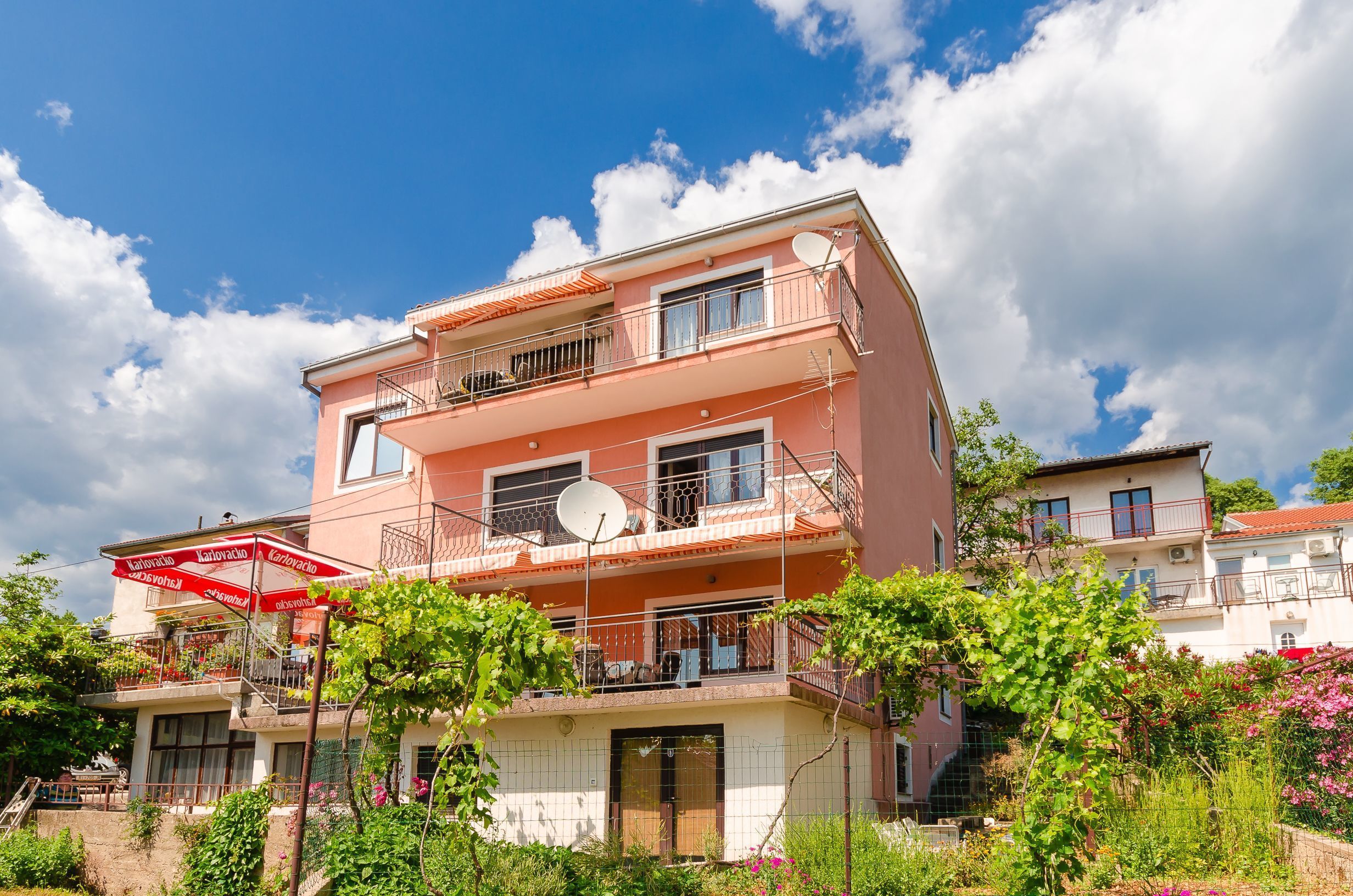 A multi-story residential building with balconies, satellite dishes, and a red awning.