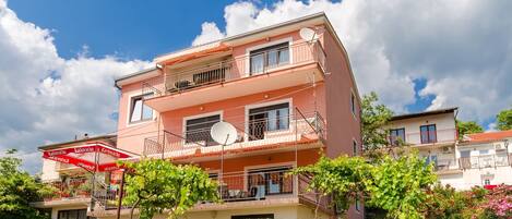 A multi-story residential building with balconies, satellite dishes, and a red awning.