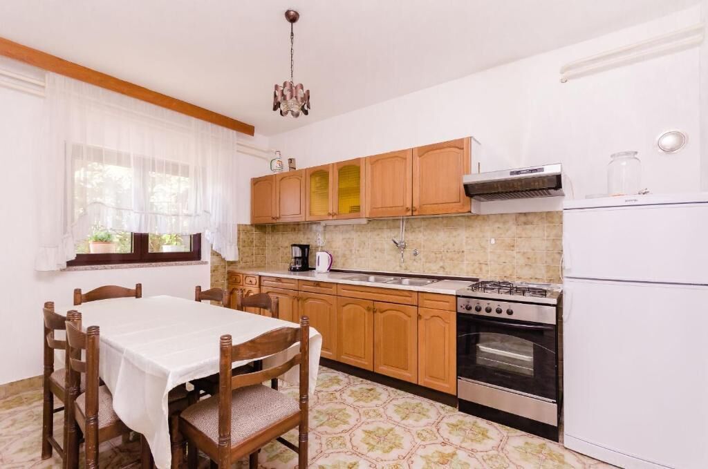 Une cuisine avec des meubles de rangement en bois, une cuisinière à gaz, un four, un évier et une table à manger avec des chaises.