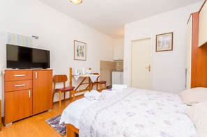 Una habitación de hotel con cama, escritorio con silla, televisor y kitchenette.