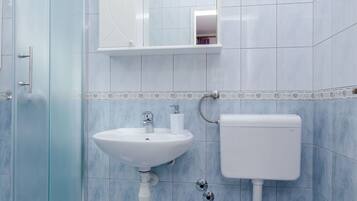 Une salle de bain avec une douche à parois de verre, un lavabo blanc, des toilettes et un miroir au-dessus du lavabo.