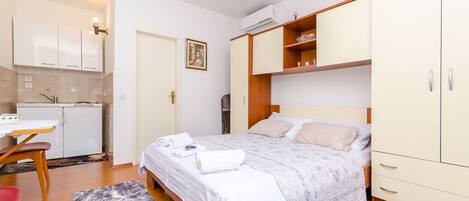 A compact bedroom with a bed, bedside tables, a wardrobe, and a kitchenette area.
