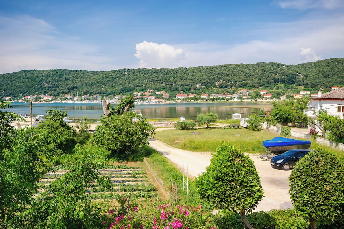A coastal town with a view of the sea, a dock, and a road leading to a parking area with a boat covered by a blue tarp.