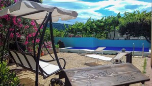 Un espace piscine comprenant deux chaises longues et une chaise suspendue, le tout entouré de verdure et adossé à un mur bleu.