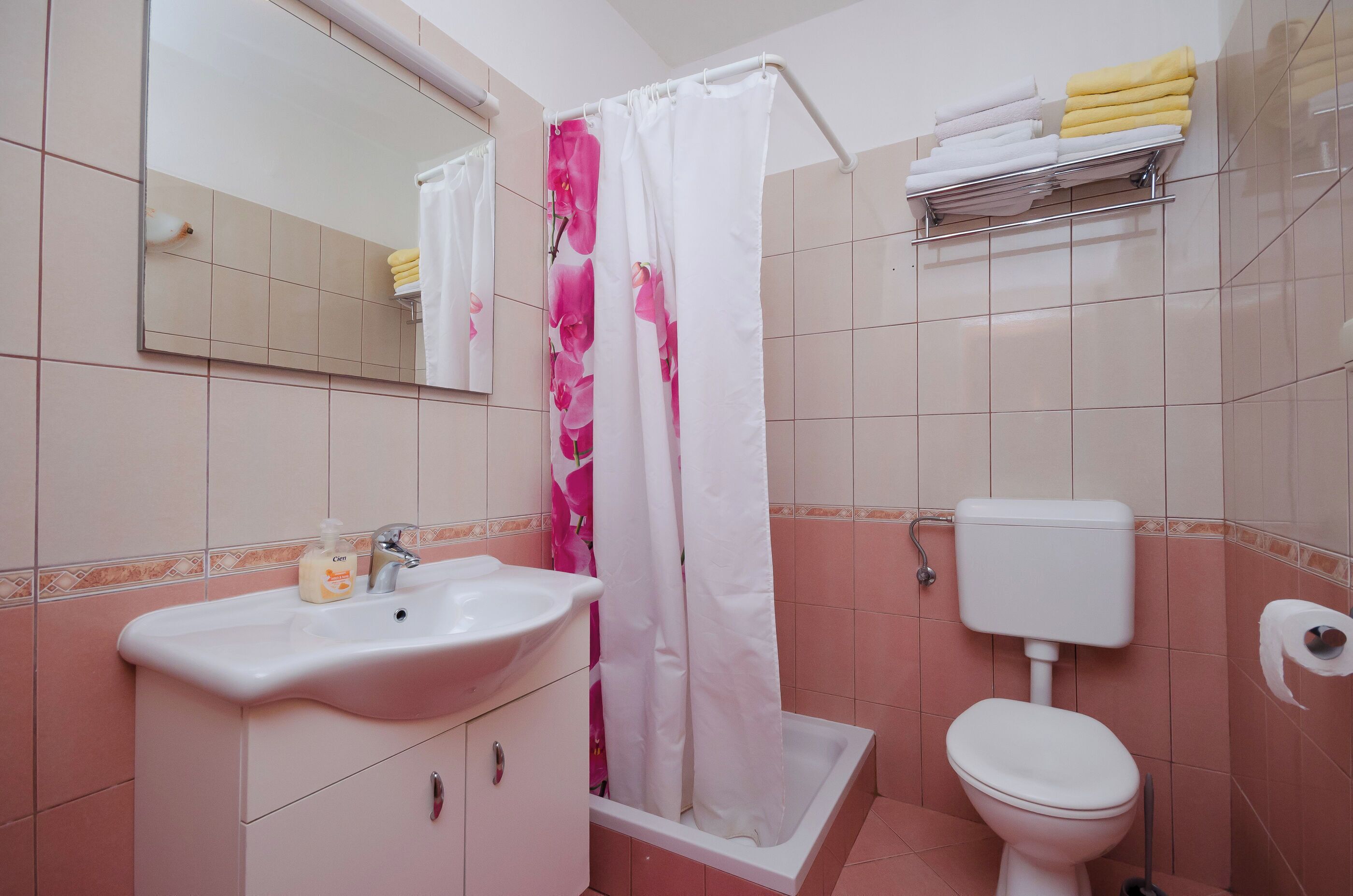 Un baño con lavamanos, espejo, inodoro, cortina de ducha y toallero.