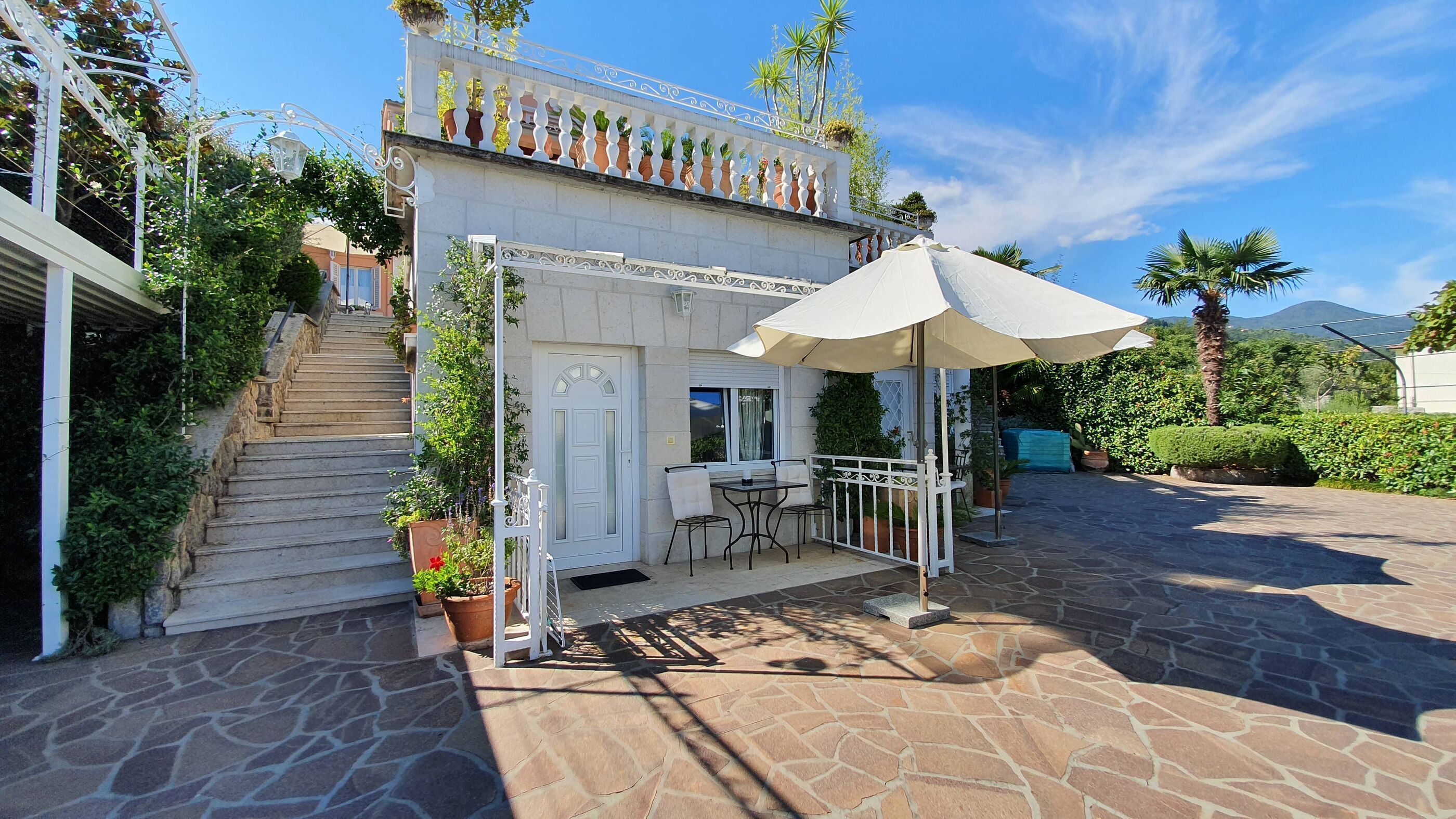 A stone-floored patio with a white door, a small table with chairs, and a large umbrella.