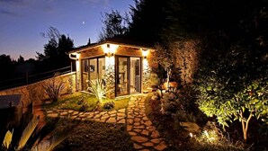 A stone-walled building with a glass door and windows, surrounded by a garden with various plants and a stone pathway. - Apartments Barbara (Lovran)