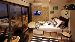 A modern living room with a sofa, a TV mounted on a textured wall, and a dining area with a table and chairs. - Apartments Barbara (Lovran)