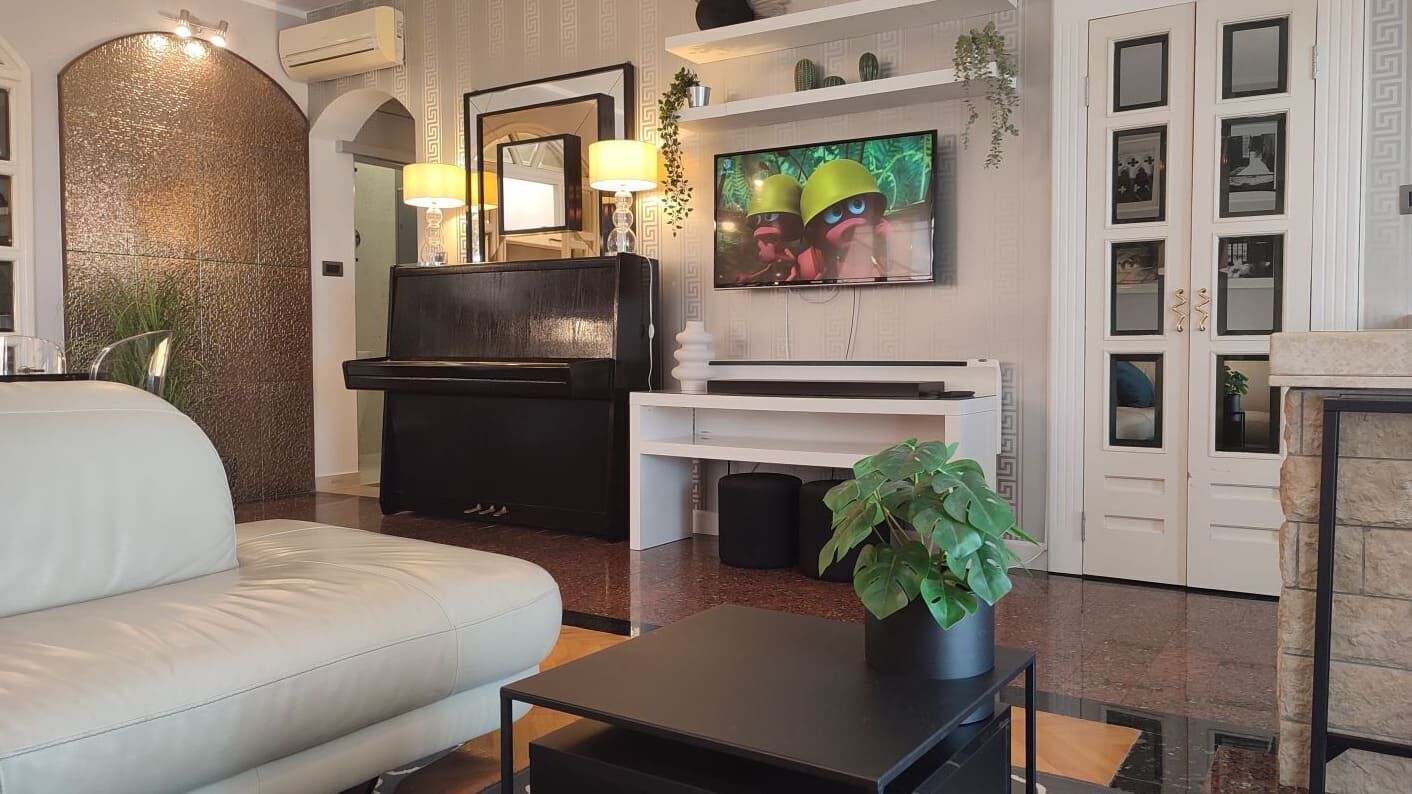 Un salon moderne avec un canapé blanc, un meuble de rangement noir, un téléviseur à écran plat et une plante en pot.