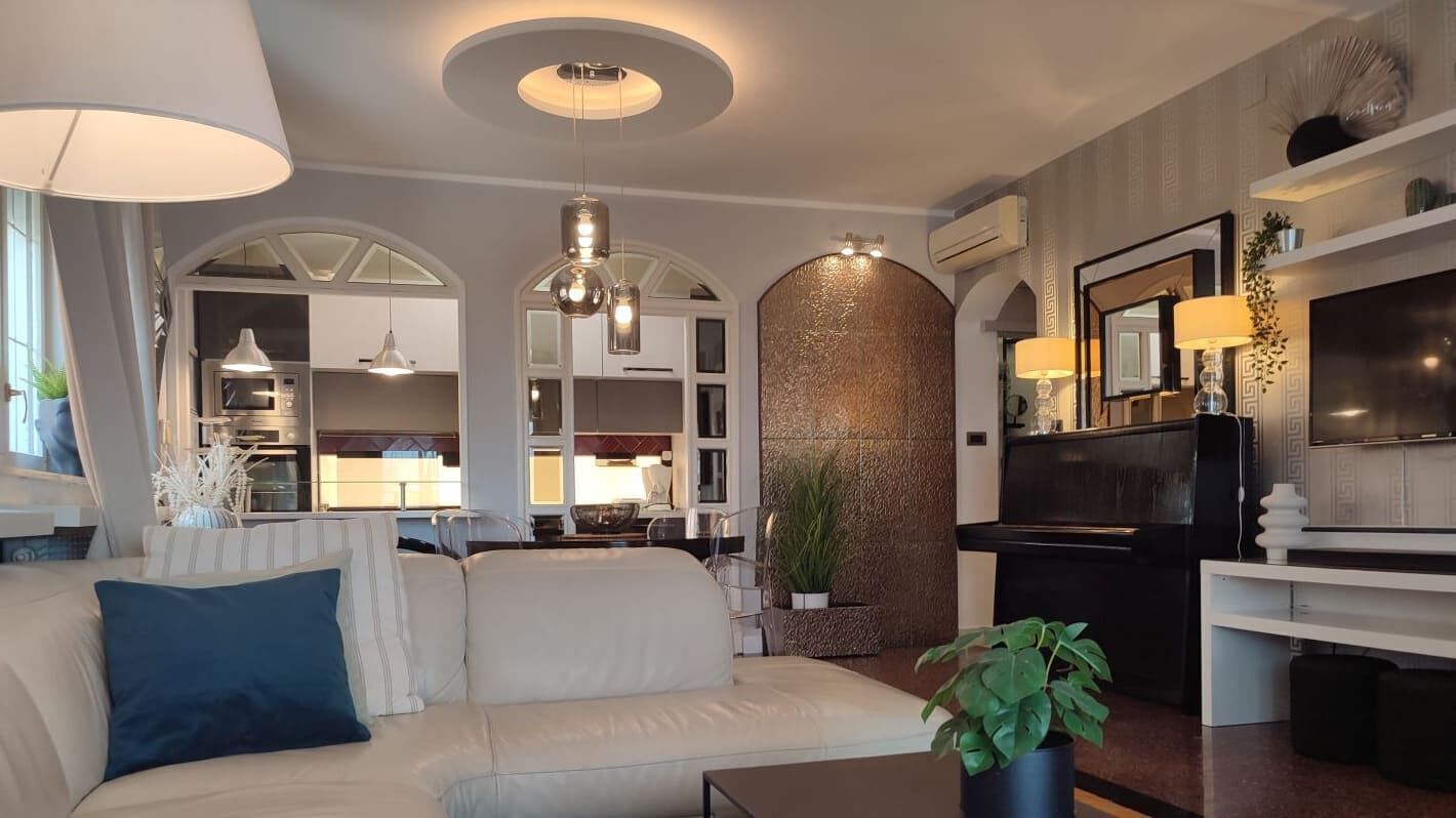 A modern living room with a sofa, a coffee table, and a TV. There is a kitchen in the background with a microwave and a stove.
