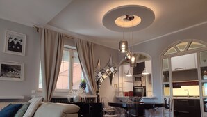 A modern living room with a sofa, a dining table with chairs, a kitchen area with appliances, and a large window with curtains. - Apartments Barbara (Lovran)