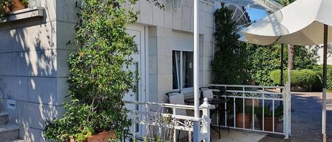 A balcony with a white railing, a potted plant, and a table with a chair.