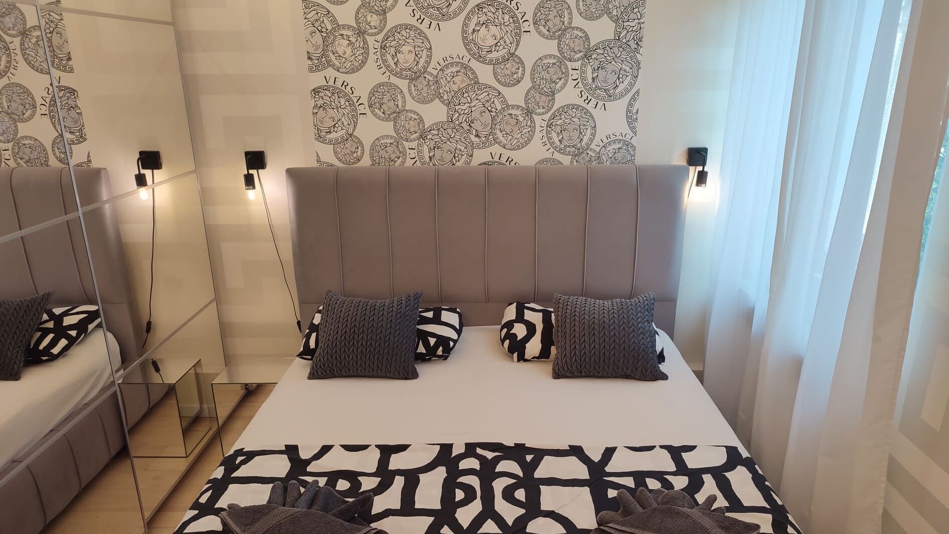 A modern hotel room with a large bed, a headboard with vertical lines, and a patterned wall.