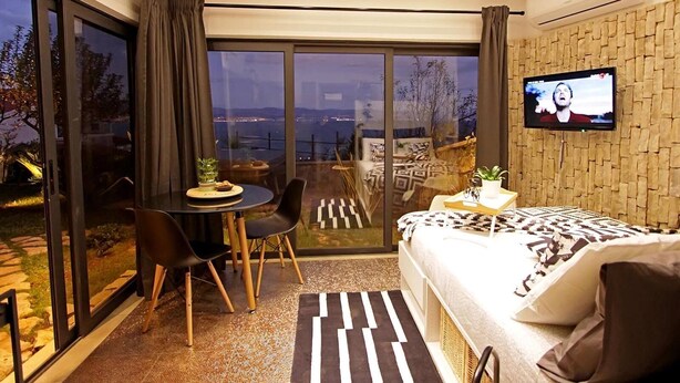 A modern bedroom with a large bed, a TV, a dining area with a table and chairs, and a view of the outdoors. - Apartments Barbara (Lovran)