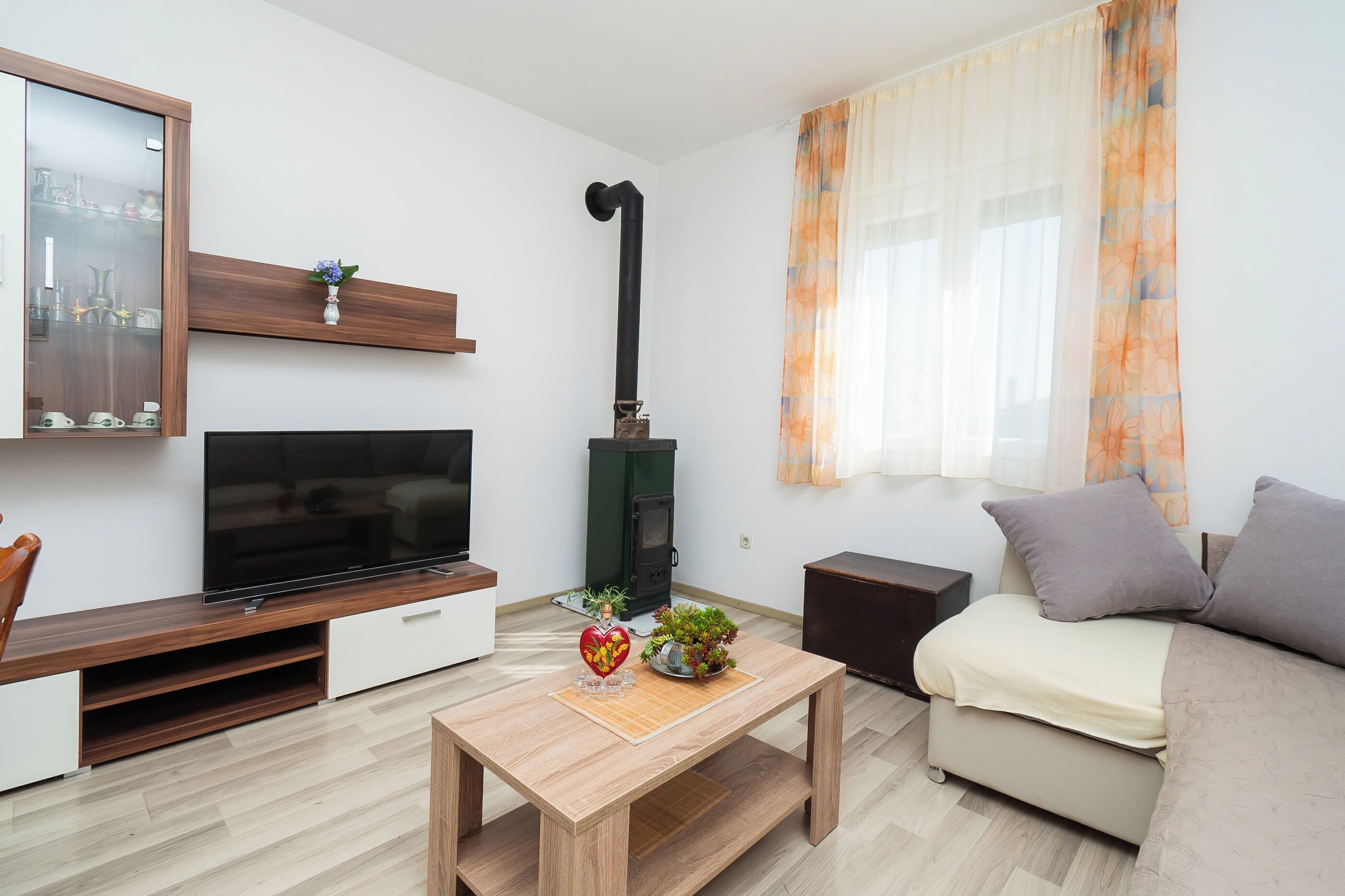 A modern living room with a flat-screen TV, wooden entertainment unit, a small table with decorative items, a sofa, and a fireplace.