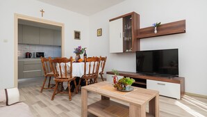 A modern living room with a wooden dining table, chairs, a TV, and a kitchen in the background. - Apartment Summerteracea (Vodice)
