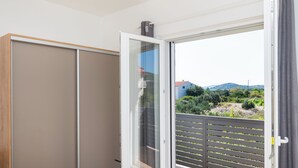 A room with a sliding glass door leading to a balcony with a view of greenery and buildings. - Apartment Summerteracea (Vodice)