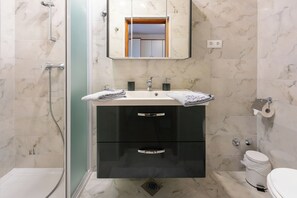 Ett modernt badrum med en dusch med glasväggar, en tvättställ med två blandare och en toalett.