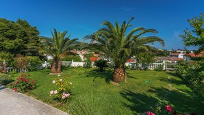 Un jardin bien entretenu, agrémenté de palmiers, d’une pelouse et d’un chemin menant à une clôture blanche.